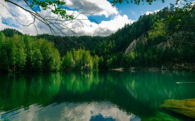 Emerald lake reflecting lush forest and cloudy sky in dolni adrspach, czech republic clipart