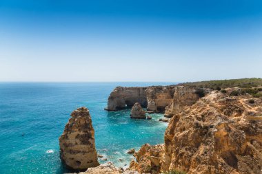 Açık mavi gökyüzünün altında turkuaz sulardan yükselen Ponta da Piedade kaya oluşumlarının nefes kesici görüntüsü lagoa, algarve, Portekiz 'de büyüleyici bir deniz manzarası yaratıyor.