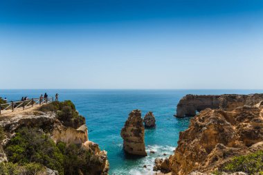 Ponta da piedade kaya oluşumlarının ve kayalıkların güneşli Algarve, Portekiz 'de güneşli bir günde turkuaz atlantik okyanusla buluşmasının panoramik manzarasından hoşlanan turistler