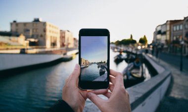 Portekiz 'in Aveiro şehrinde gün batımında renkli tekne ve evlerin fotoğrafını çekmek için akıllı telefonları tutan güzel bir anı yakalıyoruz. Canlı şehir manzarası ve mimarisi sergileniyor