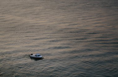 Gün batımında sakin bir denizde sakin bir şekilde seyreden küçük motorlu tekne suda rahatlatıcı dalgalar yaratıyor. Sahne huzurlu ve huzurlu, huzur ve rahatlama çağrıştırıyor.