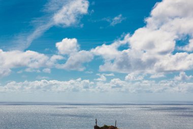 Naziler, Portekiz ve Portekiz 'de tüylü beyaz bulutlarla dolu dinamik bir gökyüzü altında parıldayan engin okyanus manzarası huzur ve resim gibi bir deniz manzarası yaratıyor. Bir kayanın tepesinde duran kişi.
