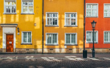 Güneş ışığı renkli binaları aydınlatıyor. Polonya 'nın gdansk şehrinde bir sokak lambasıyla kaldırım taşı caddesine gölge düşürüyor. Canlı bir şehir manzarası yaratıyor.