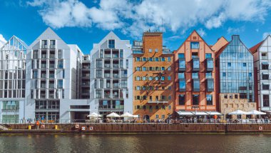 Gdansk 'taki motlawa nehrinin kıyısında duran modern ve tarihi binaların renkli cepheleri. Turistler güneşli yaz günlerinde açık hava kafelerinde yürüyüp dinleniyorlar.