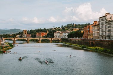 Several rowing teams are training on the arno river in florence with ponte san niccolo and typical florentine buildings in the background clipart