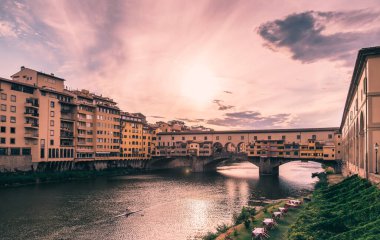 Günbatımında Arno Nehri 'ni yansıtan Ponte vecchio Floransa' da bulutlu bir gökyüzünün altında kürek eğitimi ve renkli binalar.