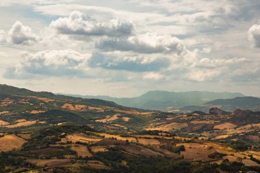 Ekilmiş tarlalar ve yuvarlanan tepeler bulutlu bir gökyüzünün altında San Marino kırsalının doğal güzelliğini gözler önüne seren pitoresk bir manzara yaratır.
