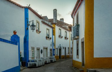 Portekiz 'in tarihi Obidos kasabasında dolambaçlı kaldırım taşı caddesinde mavi ve sarı aksanlı büyüleyici beyaz evler ve demir balkonlar vardı.