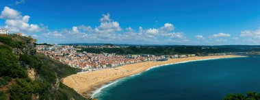 Portekiz 'de güzel bir yaz gününde kayalıklar ve okyanus arasında uzanan altın kumlar, turkuaz sular ve büyüleyici şehir manzarası ile Nazi sahilinin nefes kesici panoramik manzarası.