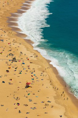 Portekiz 'deki Naziler' in kumsalının havadan görünüşü. Turistlerle dolu. Kumda güneşlenmenin ve okyanusta yıkanmanın tadını çıkarıyorlar.