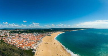 Praia de Nazare 'nin altın kumları ve mavi suları kabarık bulutları olan canlı bir gökyüzünün altında büyüleyici bir şehir.