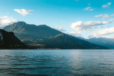 Como Gölü kıyı şeridi boyunca uzanan görkemli dağlarla mavi gökyüzünü ve büyüleyici köyü yansıtarak Lombardy, İtalya 'da güzel bir manzara yarattı.