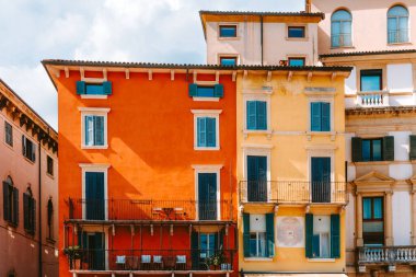 Verona 'nın Giardini Vittorio Emanuele II' sinde mavi panjurlu renkli binalar. Parlak bir gökyüzü altında canlı turuncu ve sarı cepheler klasik İtalyan mimari tarzını sergiliyor.