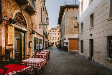 İtalya Treviso 'da kırmızı ve beyaz masa örtüleri olan samimi açık hava restoranları Treviso' da büyüleyici bir kaldırım taşı caddesi, yoldan geçenleri tarihi şehir merkezinde yemek yemeye davet ediyor.