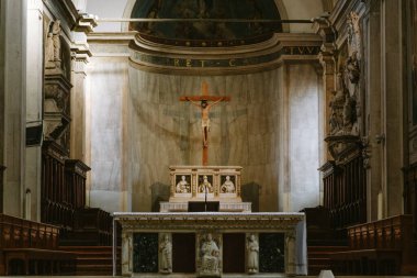 İtalya Treviso Katedrali 'nin içinde haç ve sunak aydınlatan güneş ışığı güneşli bir günde dini heykeller, mimari ve ruhani atmosfer sergiliyor.