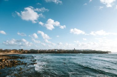 Peniche, Portekiz 'in arka planında bulutlu bir gökyüzünün altında kayalık sahile çarpan dalgalar güzel bir kıyı sahnesi oluşturur.