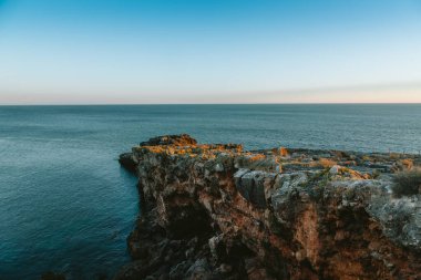 Altın saat güneş ışığı, Portekiz, Cascais 'in engebeli kıyı şeridini aydınlatıyor. Kayalık uçurumun engin Atlantik Okyanusu' na doğru ilerlemesiyle dramatik bir sahne yaratıyor.