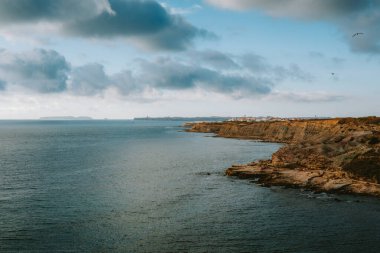 Kayalık kıyı şeridi, Atlantik Okyanusu 'nun uçsuz bucaksız genişliğiyle çarpıcı, bulutlu gökyüzünün altında birleşerek Portekiz kıyılarının nefes kesici manzarasını sunuyor.