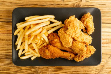 Breaded Fried Chicken Wings, Fingers and Drumsticks on Wooden Rustic Background Top View. Hot Crispy Chicken Nuggets, French Fries, Fillet Strips, Meat Pieces in Breadcrumbs