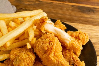 Breaded Fried Chicken Wings, Fingers and Drumsticks on Wooden Rustic Background Closeup. Hot Crispy Chicken Nuggets, French Fries, Textured Fillet Strips, Meat Pieces in Breadcrumbs