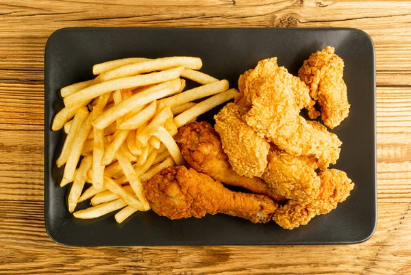 Breaded Fried Chicken Wings, Fingers and Drumsticks on Wooden Rustic Background Top View. Hot Crispy Chicken Nuggets, French Fries, Fillet Strips, Meat Pieces in Breadcrumbs
