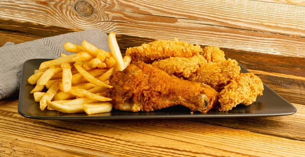 Breaded Fried Chicken Wings, Fingers and Drumsticks on Wooden Rustic Background Side View. Hot Crispy Chicken Nuggets, French Fries, Fillet Strips, Meat Pieces in Breadcrumbs