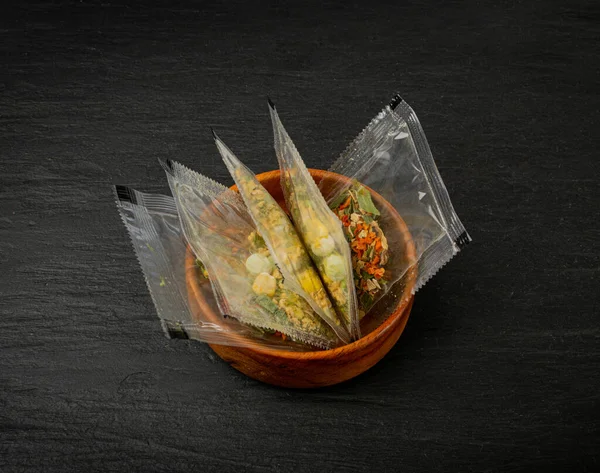 Small Spice Pouch on Black Background, Dried Vegetables and Herbs Mix in Plastic Bag, Dry Peas, Greens, Dehydrated Food Pieces