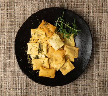 Pita Chips Pile on Black Plate, Small Wheat Tortillas, Crunchy Flat Bread with herbs and Spipices, Spicy Mediterranean Wheat Snack, Pita Chips Top View