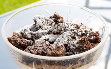 Çikolatalı kek parçacıkları üzerine pudra şekeri serpiştirilmiş, Tiramisu porsiyonu küçük bir vazoda, parçalanmış çikolatalı pasta kapağı