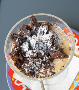 Çikolatalı kek parçacıkları üzerine pudra şekeri serpiştirilmiş, Tiramisu porsiyonu küçük bir vazoda, parçalanmış çikolatalı pasta kapağı