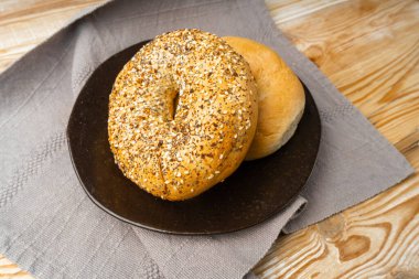 Tahta bir masada simit, iki yuvarlak ekmek ekmeği, tahıllı buğday fırını ve kahvaltı için tohumlar, gri bir peçete arkaplanındaki yuvarlak simit ekmeği.