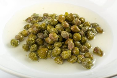 Salamura kapari salamura halinde. Terbiye edilmiş kapari tomurcukları, küçük tuzlu kapuçinler, mayalanmış yiyecekler, beyaz arka planda turşulu kapari grubu.