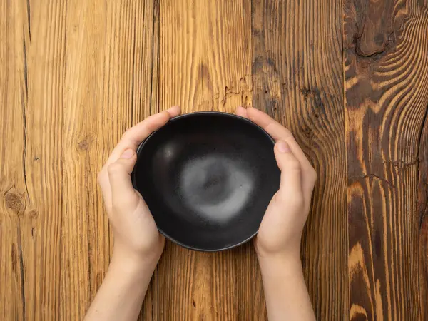 Bowl in Hands, Empty Bowl in Arms on Wooden Background, Vintage Kitchen Tableware Mockup, Dishware Banner, Empty Plate, Starving, Hungry Concept, Black Ceramic Bowl with Copy Space for Text