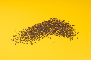 Çikolata serpintisi, çikolata serpintisi, şeker serpintisi, tatlı kahverengi gevrek süsleme, çikolata vermicelli, sarı arka plan üst görünümü