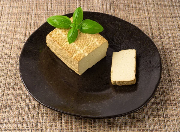 Tofu Cheese Block, Smoked Vegan Cheese Slice on Black Plate, Sliced Soya Bean Curd, Soy Protein or TSP Healthy Meat Analogue, Tofu Cheese on Rustic Background