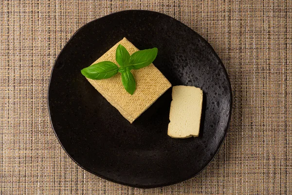 Tofu Cheese Block, Smoked Vegan Cheese Slice on Black Plate, Sliced Soya Bean Curd, Soy Protein or TSP Healthy Meat Analogue, Tofu Cheese on Rustic Background