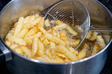 Kaynar yağda patatesler, ev yapımı patates kızartmaları, metal tavada kızartılmış patatesler, yağlı fast food pişirme, yağlı baloncuk dokusu yakın çekim.