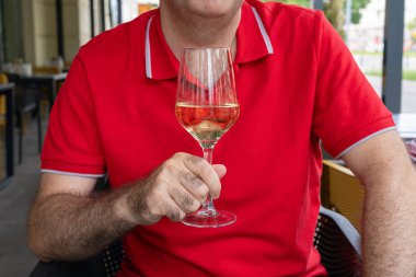 Kırmızı arka planda beyaz şarap kadehi yakın plan. Bir bardak beyaz şarap tutan bir adam, kırmızı gömlek giyen bir adamın yakın plan görüntüsü, yaz aylarında dışarıda dinlenen