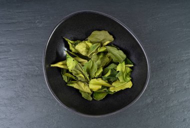 Tayland kireç kuru yaprakları, kireç taşı veya Citrus hystrix yaprağı yığını, kaffir limon kuru lahanası, Güneydoğu Asya baharatları, siyah arka planda Tom yer elması çorbası malzemesi.
