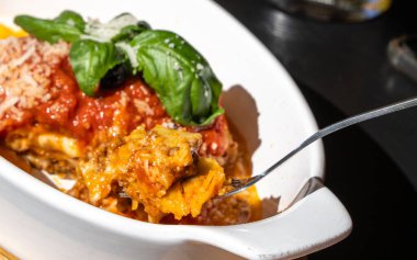 Lazanya porsiyonu, fırında lazanya, peynirli makarna, kıyma, domates. Güneşli bir yaz gününde, sokak restoranındaki masada lazanya, bulanık bir arka plan.