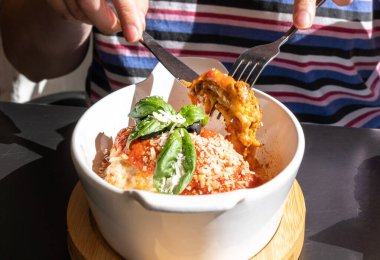 Lazanya porsiyonu, fırında lazanya, peynirli makarna, kıyma, domates. Güneşli bir yaz gününde, sokak restoranındaki masada lazanya, bulanık bir arka plan.