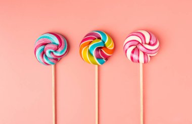 Renkli lolipop, çubukta sarmal şeker, renkli çizgili lolipop, yuvarlak meyveli karamel, çok renkli şekerleme, pembe arka planda daire şeklinde lolipop, metin için kopyalama alanı