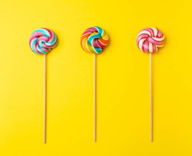 Renkli lolipop, çubukta sarmal şeker, renkli çizgili lolipop, yuvarlak meyveli karamel, çok renkli şekerleme, sarı arka planda daire şeklinde lolipop, metin için kopyalama alanı