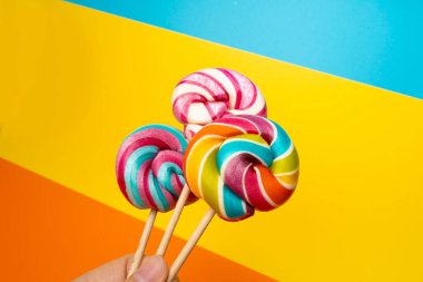 Renkli lolipop, çubukta sarmal şeker, renkli çizgili lolipop, yuvarlak karamelli meyve, renkli şekerleme, turuncu arka planda daire şeklinde lolipop, metin için kopyalama alanı