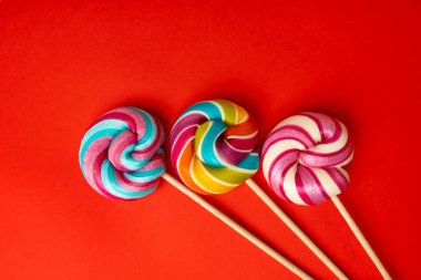 Renkli lolipop, çubukta sarmal şeker, renkli çizgili lolipop, yuvarlak meyveli karamel, çok renkli şekerleme, kırmızı arka planda daire şeklinde lolipop, metin için kopyalama alanı