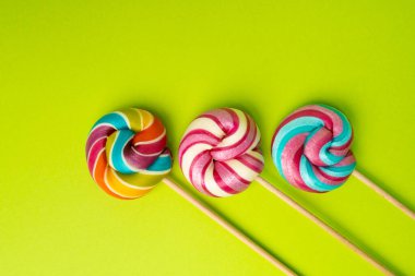 Renkli lolipop, çubukta sarmal şeker, renkli çizgili lolipop, yuvarlak meyveli karamel, çok renkli şekerleme, yeşil arka planda daire lolipop, metin için kopyalama alanı
