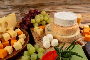 Cheese plate of color cheeses variety, yellow, white and blue gorgonzola platter, munster, fourme cheese board, assorted chopped dairy products, many stinky French cheeses on wood clipart