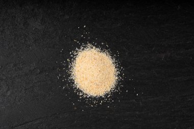 Sarımsak tozu, kurumuş granüle edilmiş ezilmiş sarımsak karanfilleri, küçük parçalara bölünmüş gıda malzemeleri, siyah arka planda baharat.