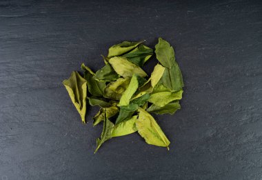 Thai lime dried leaves, makrut lime or Citrus hystrix leaf pile, kaffir lime dry sprouts, Southeast Asia spices, tom yam soup ingredient on black background clipart