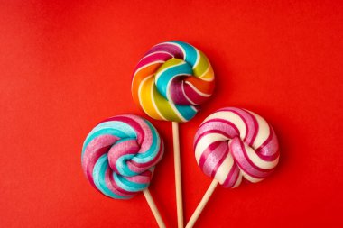 Renkli lolipop, çubukta sarmal şeker, renkli çizgili lolipop, yuvarlak meyveli karamel, çok renkli şekerleme, kırmızı arka planda daire şeklinde lolipop, metin için kopyalama alanı